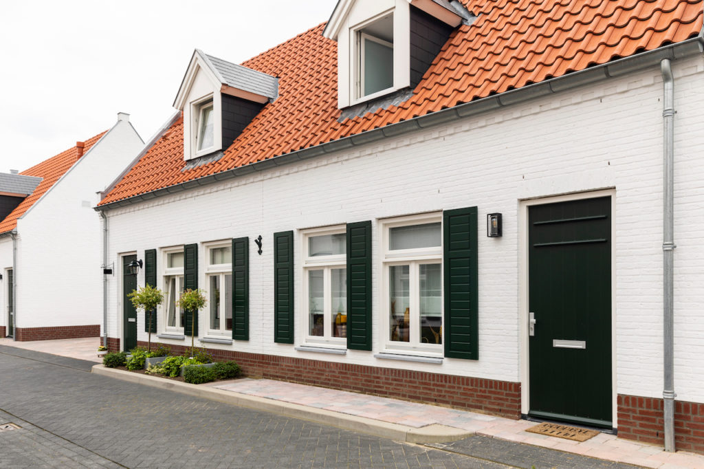 White modern houses with an orange roof in Thorn, Limburg, The Netherlands, a village known for its white houses and buildings. Green shutters next to the windows, greenery and plants in front