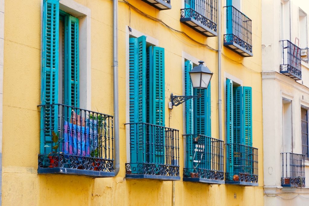 Tiny balconies with vivid blue shutters on vibrant yellow wall. Weathered facades in Lavapies district downtown Madrid, Spain.