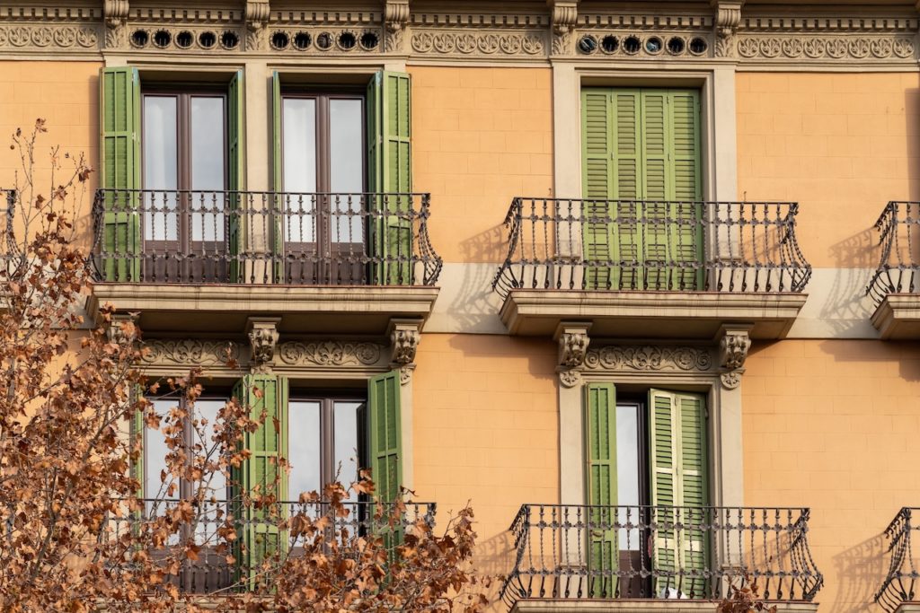 Traditional Barcelona style balconies and green wooden shuttered windows on facade of the renovated house on a sunny day, in the old city of the center.