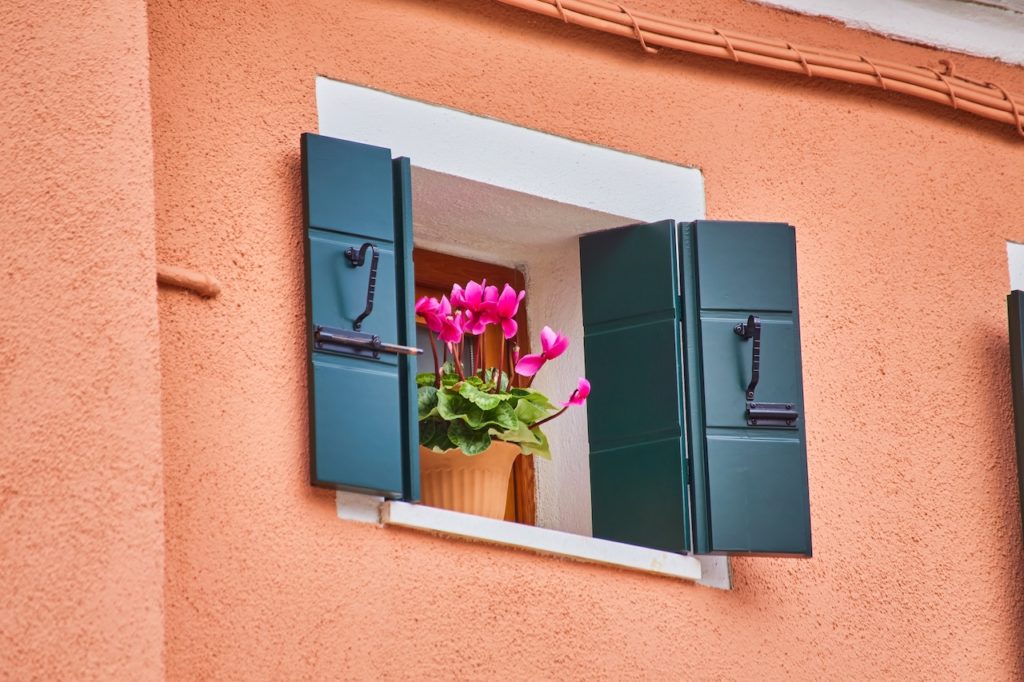 Window with brown shutters and flowers in the pot. Italy, Venice, Burano